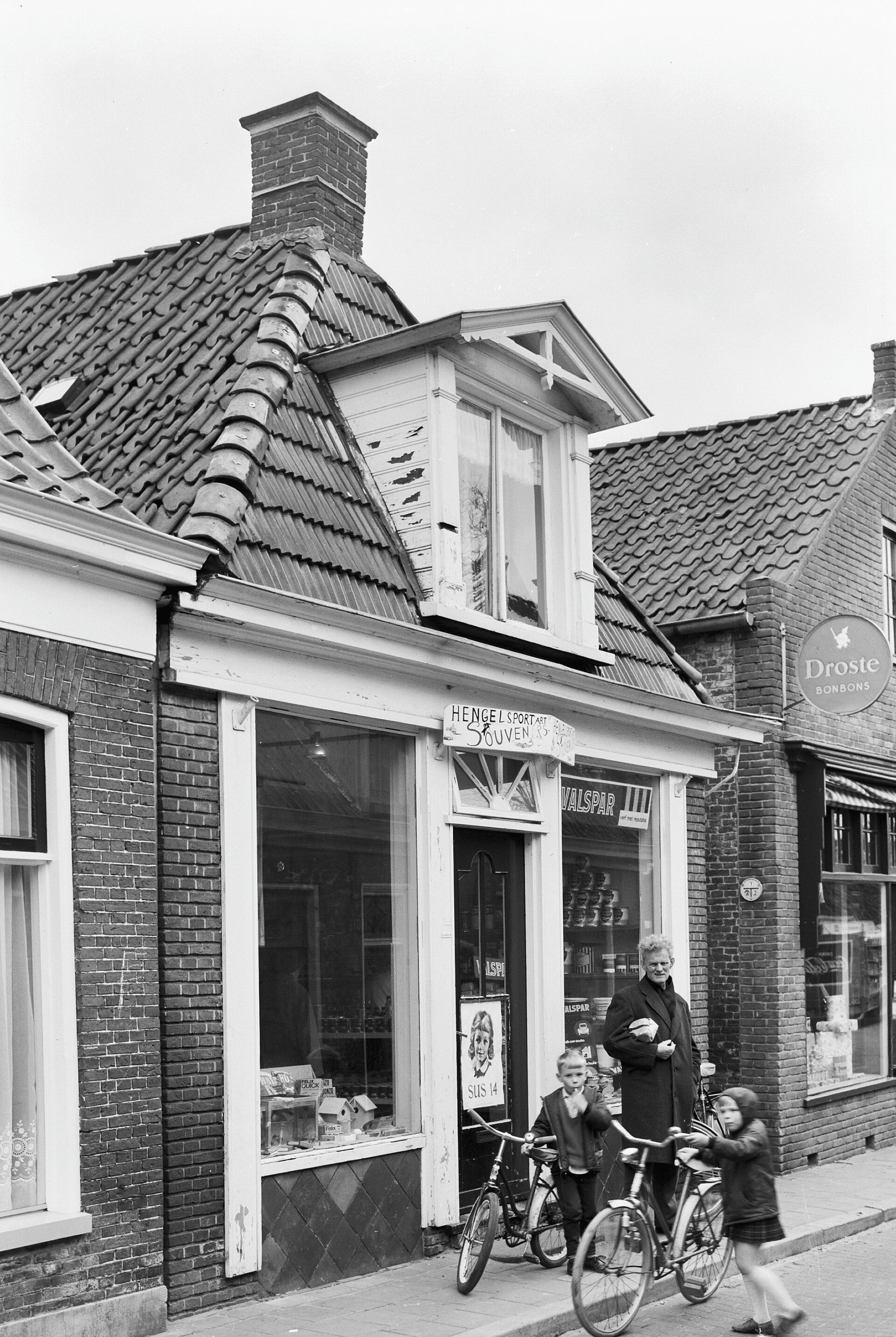 Winkel in hengelsportartikelen en souvenirs in Grouw, 1967, met een klant en twee kinderen met fietsen voor de etalage